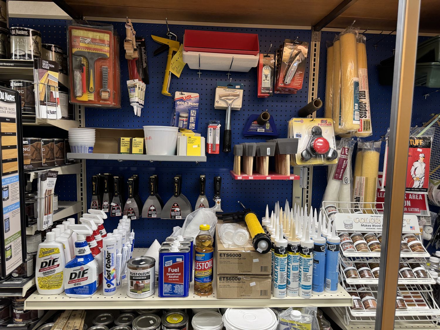 A pegboard of wallpaper tools, caulk, putty knives, and Zinsser DIF wallpaper stripper